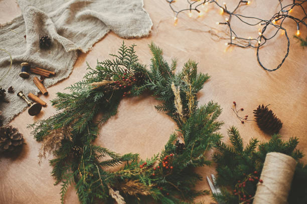 istock Rustic Christmas wreath. Fir branches, pine cones, thread, berries, cinnamon and golden lights on wooden table. Christmas wreath workshop. Authentic stylish still life 1177462283
