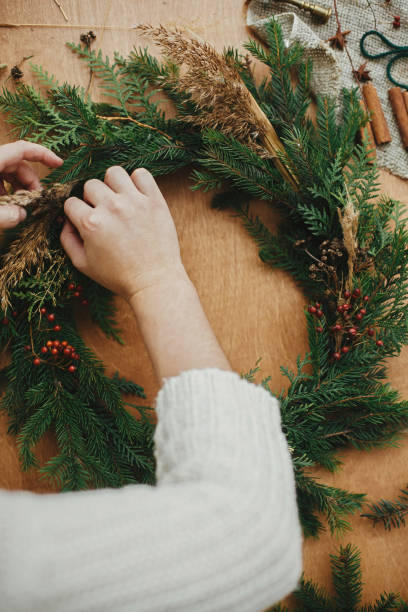 istock Making rustic Christmas wreath flat lay. Hands holding berries and  fir branches, pine cones, thread on wooden table. Christmas wreath workshop. Authentic stylish still life. 1177462301