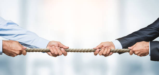 Tug of war, two businessman pulling a rope in opposite directions Tug of war, two businessman pulling a rope in opposite directions over defocused background with copy space rivalry stock pictures, royalty-free photos & images