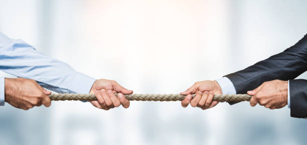 Tug of war, two businessman pulling a rope in opposite directions Tug of war, two businessman pulling a rope in opposite directions over defocused background with copy space business battle stock pictures, royalty-free photos & images