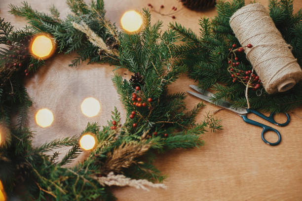 istock Rustic Christmas wreath. Fir branches, pine cones, thread, berries, scissors and golden lights bokeh on wooden table. Christmas wreath workshop. Authentic stylish still life 1177463122