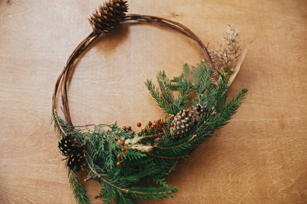 istock Christmas rustic wreath. Creative rural christmas wreath with fir branches, berries, pine cones and herbs on wooden table. Copy space. Season's greetings. 1177463695