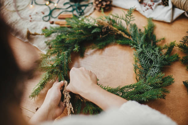 istock Making rustic Christmas wreath. Hands holding herbs and fir branches, pine cones, thread, berries, cinnamon on wooden table. Christmas wreath workshop. Authentic stylish still life. 1177463928