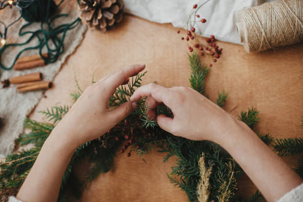 istock Hands holding fir branches, and pine cones, thread, berries, scissors on wooden table. Making rustic Christmas wreath flat lay. Christmas wreath workshop. Authentic stylish still life 1177464174