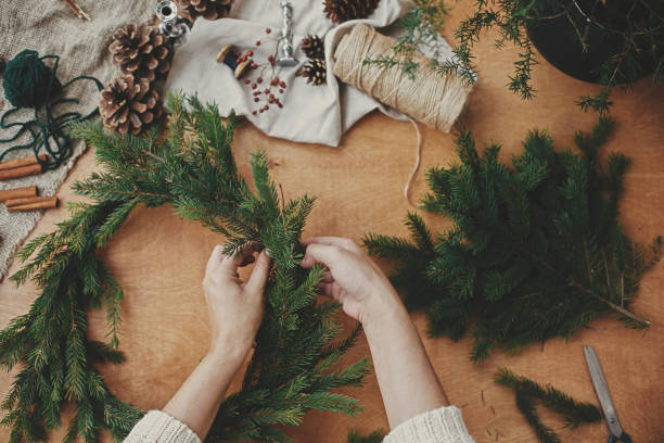 istock Making rustic Christmas wreath flat lay. Hands holding fir branches, and pine cones, thread, berries, scissors on wooden table. Christmas wreath workshop. Authentic stylish still life 1177464307