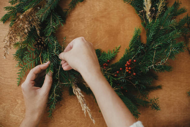 istock Making rustic Christmas wreath flat lay. Hands holding fir branches, and pine cones, thread, berries  on wooden table. Christmas wreath workshop. Authentic stylish still life 1177465471