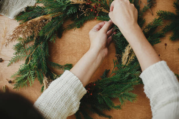 istock Making rustic Christmas wreath flat lay. Hands holding berries and  fir branches, pine cones, thread on wooden table. Christmas wreath workshop. Authentic stylish still life. 1177465497