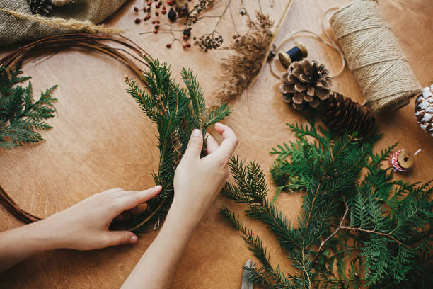 istock Hands holding fir branches and pine cones, thread, scissors on wooden table. Details for workshop of making christmas wreath. Making rustic christmas wreath 1177465521