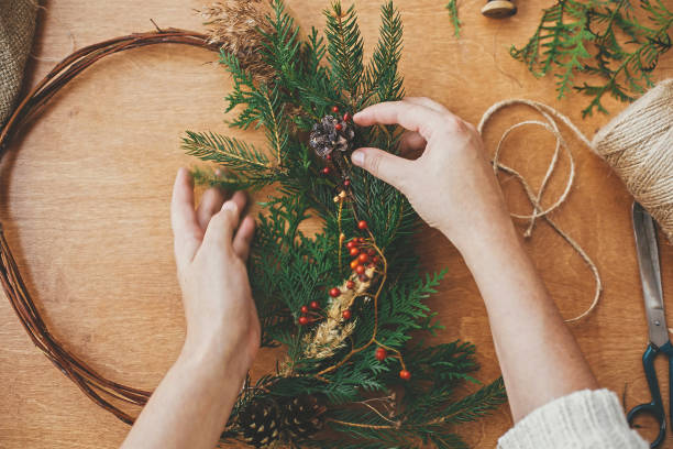istock Making rustic christmas wreath flat lay. Hands holding fir branches and pine cones, berries, thread, scissors on wooden table. Details for workshop of making christmas wreath 1177465550