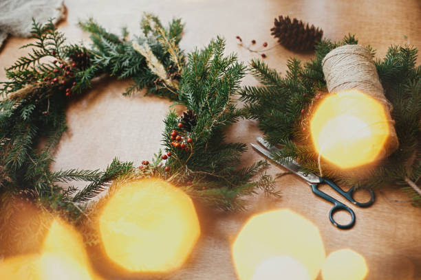 istock Rustic Christmas wreath. Fir branches, pine cones, thread, berries, scissors and golden lights bokeh on wooden table. Christmas wreath workshop. Authentic stylish still life 1177465631
