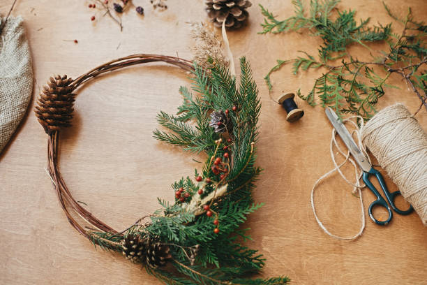 istock Rustic Christmas wreath. Creative christmas wreath with fir branches, berries, pine cones and herbs with scissors and thread on rural wooden table. Happy holidays. Workshop 1177465672