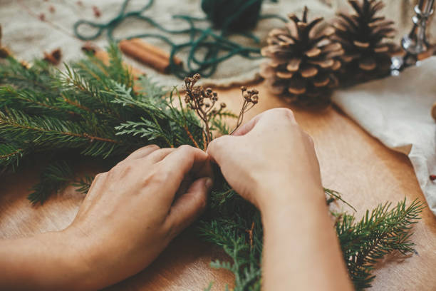 istock Hands holding herbs and  fir branches, pine cones, thread, berries, cinnamon on wooden table. Christmas wreath workshop. Authentic stylish still life. Making rustic Christmas wreath. 1177465750