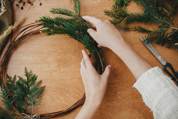 istock Hands holding fir branches and pine cones, thread, scissors on wooden table. Details for workshop of making christmas wreath. Making rustic christmas wreath flat lay. 1177466365