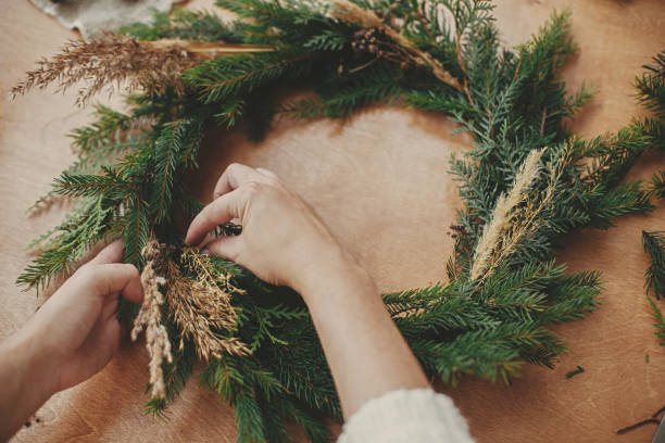 istock Hands holding herbs and  fir branches, pine cones, thread, berries, cinnamon on wooden table. Christmas wreath workshop. Authentic stylish still life. Making rustic Christmas wreath. 1177466656