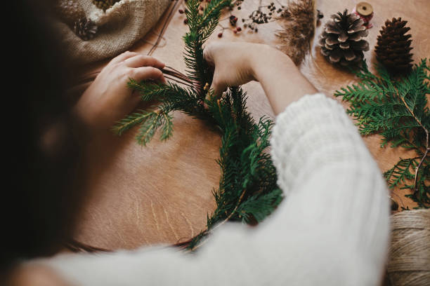 istock Girl hands holding fir branches and pine cones, thread, scissors on wooden table. Making rustic christmas wreath. Details for workshop of making christmas wreath 1177467259