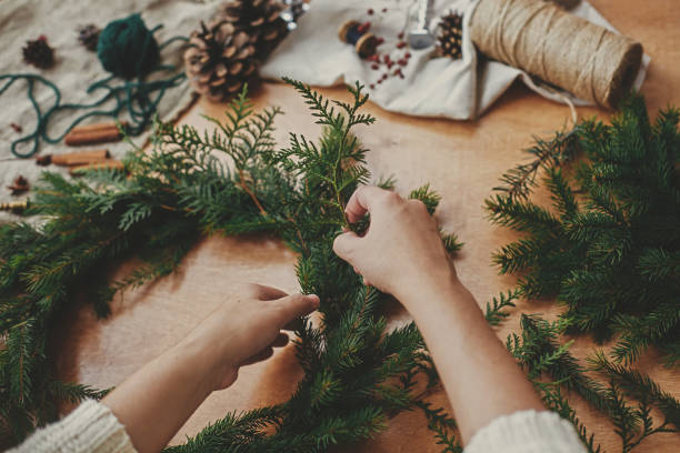 istock Hands holding fir branches, and pine cones, thread, berries, scissors on wooden table. Christmas wreath workshop. Authentic stylish still life. Making rustic Christmas wreath. 1177467468