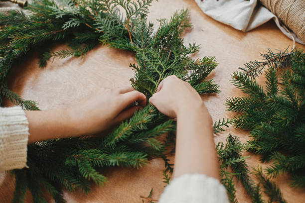 istock Making rustic Christmas wreath. Hands holding fir branches, and pine cones, thread, berries, scissors on wooden table. Christmas wreath workshop. Authentic stylish still life 1177467636