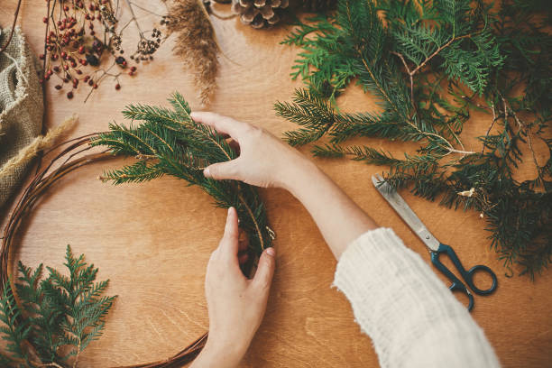 istock Making rustic christmas wreath flat lay. Hands holding fir branches and pine cones, thread, scissors on wooden table. Details for workshop of making christmas wreath 1177467904