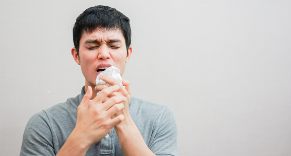 close up young asian man sneezing after get allergy or flu virus and using tissue paper for swipe on nose at home after wake up for unhealthy lifestyle concept