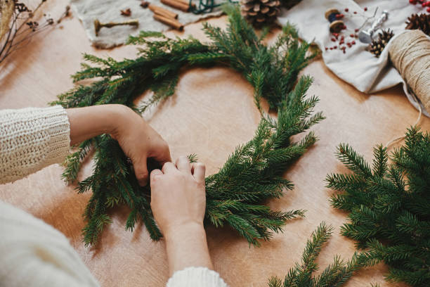 istock Making rustic Christmas wreath. Hands holding fir branches, and pine cones, thread, berries, scissors on wooden table. Christmas wreath workshop. Authentic stylish still life 1177468003