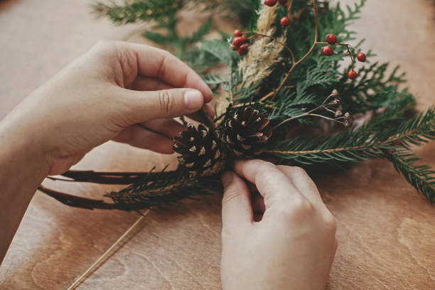 istock Making rustic christmas wreath. Hands holding pine cones, berries, fir branches, thread, scissors on wooden table.  Authentic rural wreath. Christmas wreath workshop 1177468325