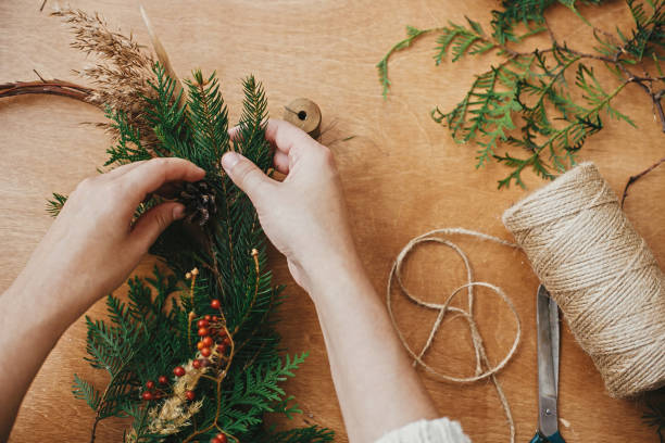 istock Hands holding fir branches and pine cones, berries, thread, scissors on wooden table. Making rustic christmas wreath flat lay. Details for workshop of making christmas wreath 1177468433