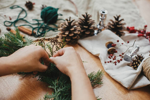 istock Making rustic Christmas wreath. Hands holding herbs and  fir branches, pine cones, thread, berries, cinnamon on wooden table. Christmas wreath workshop. Authentic stylish still life. 1177469016