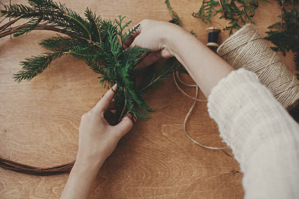 istock Making rustic christmas wreath flat lay. Hands holding fir branches and pine cones, thread, scissors on wooden table. Details for workshop of making christmas wreath 1177469407