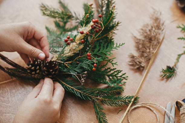 istock Making rustic christmas wreath. Hands holding pine cones, berries, fir branches, thread, scissors on wooden table.  Authentic rural wreath. Christmas wreath workshop 1177469434
