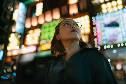 A portrait of young woman at night while looking up in the street.