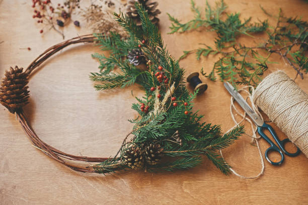 istock Rustic Christmas wreath. Creative christmas wreath with fir branches, berries, pine cones and herbs with scissors and thread on rural wooden table. Happy holidays. Workshop 1177469598