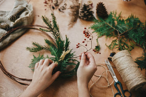 istock Making rustic christmas wreath. Hands holding berries, fir branches, pine cones, thread, scissors on wooden table.  Authentic rural wreath. Christmas wreath workshop 1177469686