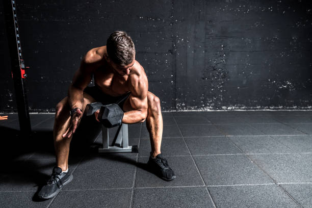 młody silny muskularny spocony dopasować człowieka biceps mięśni trening krzyżowy trening z ciężkim hantle w siłowni ciemny obraz z cieniami prawdziwych ludzi - shirtless energy action effort zdjęcia i obrazy z banku zdjęć