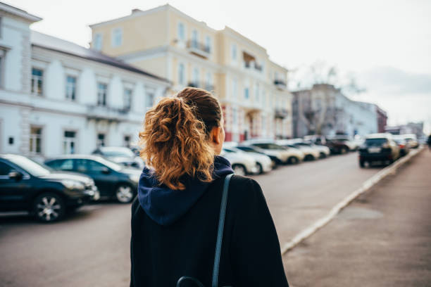 donna con i capelli ricci in un cappotto nero cammina - ponytail brown hair tourist women foto e immagini stock