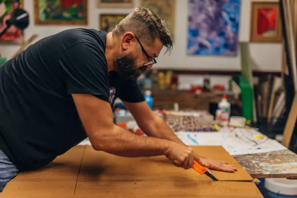 Male artist in his studio, cutting canvas with scalpel.