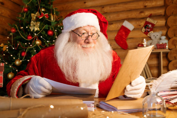 istock Santa with white beard sitting by table while looking at envelope in his hand 1177491741