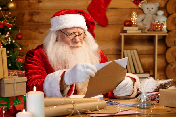 istock Serious Santa sitting by table at home and putting letter into envelope 1177491749
