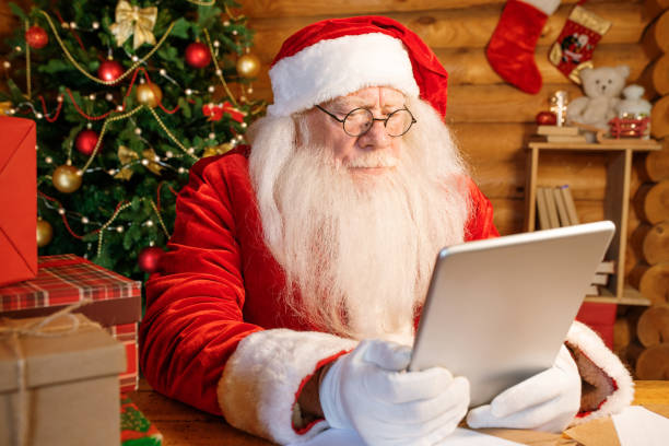istock Serious Santa sitting at home by wooden table with tablet in front 1177491860