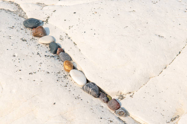 istock Small beach pebbles in a row on a rocky white surface. 1177493669