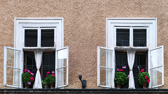 Two open windows with colorful flowers in autumn Salzburg