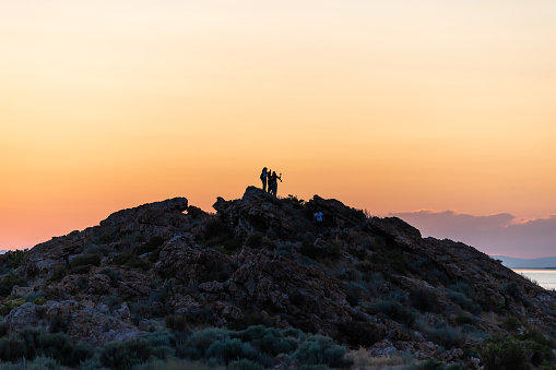 Syracuse, USA - July 28, 2019: Silhouette of people on top of cliff looking at sunset orange yellow sunlight on Great Salt Lake in Antelope Island State Park Ladyfinger trail in Utah