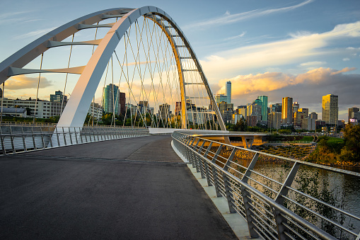 View of Edmonton, Albert, Canada skyline seen from suspension bridge with walking path and river in the foreground shot at dusk with partially cloudy sky