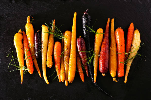 coloridas zanahorias arco iris asadas dispuestas en una fila sobre un fondo de piedra negra - roasted vegetable fotografías e imágenes de stock
