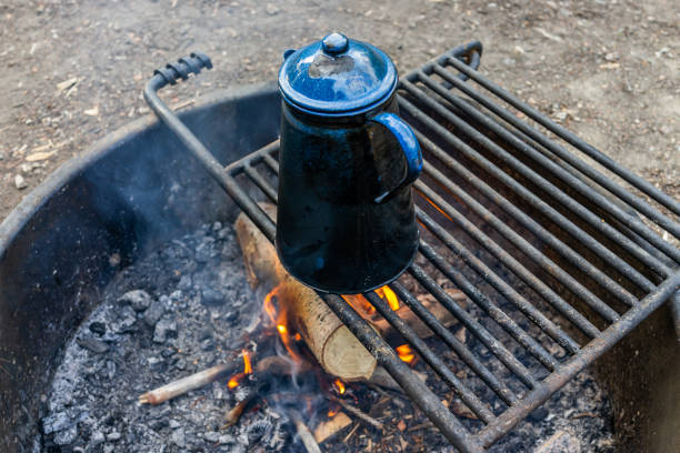 Blue tea water kettle on grill in fire pit at campground with red flame fire burning in evening