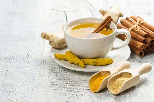 Herbal ginger and turmeric tea in white cup with ginger root, dry turmeric, cinnamon sticks and their powder stock photo