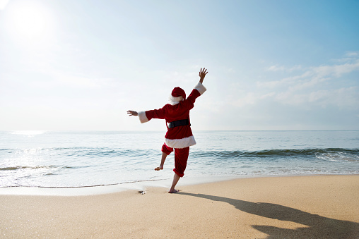 Santa Claus standing on sea beach with arms raised.