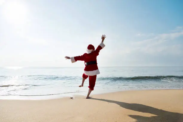 Photo of Santa Claus standing on sea beach with arms raised