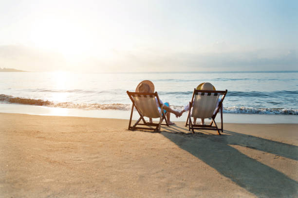 Couple sitting on deck chair at beach Couple sitting on deck chair at beach. deckchair stock pictures, royalty-free photos & images