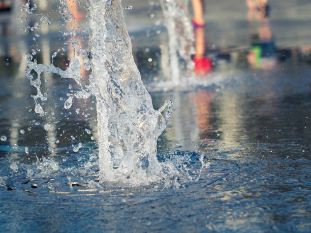 vista de cerca de las corrientes de agua que salen de la rejilla de acero inoxidable de la fuente seca. los niños se enfrían cerca de la fuente. plaza de la ciudad en verano. enfoque suave selectivo. fondo borroso. - fountain water physical pressure splashing fotografías e imágenes de stock