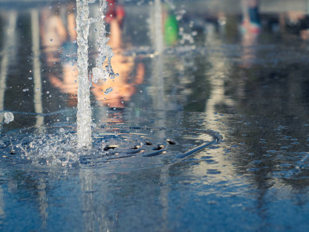 corrientes de agua que fluyen de rejilla inoxidable de fuente seca, vista de cerca. padres con niños reflexionando sobre la superficie del agua. plaza towm en verano. enfoque suave selectivo. fondo borroso. - fountain water physical pressure splashing fotografías e imágenes de stock